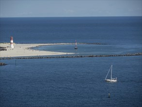 Sailboat in calm blue sea, lighthouse on beach and blue sky, Heligoland, Germany, Europe