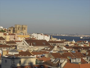 View of city with many roofs and an old tower, behind it the sea, view of the old town of Lisbon by