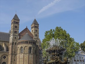 Historic church with two towers, visible against a clear blue sky, next to a fountain and green