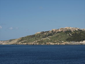 A distant city view on a green hill by the sea with a clear sky, the island of Gozo with historic