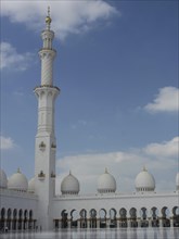 Minaret and white buildings of a mosque with arches, depicted in Islamic architecture under a blue