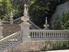 Classic stone staircase with railings and green plants, surrounded by trees, Barcelona, Spain,