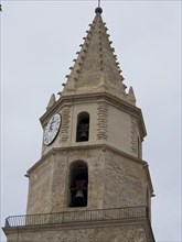 Historic sandstone bell tower with clock and bells in front of a cloudy sky, palma de Majorca with