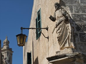 Detail of historic architecture with sculpture and street lamp, church tower in the background, the