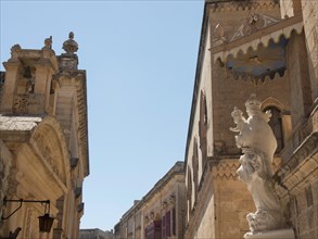 A street of historic buildings and statues under a blue sky, the town of mdina on the island of