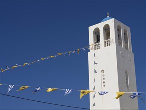 A white bell tower with decorative flags fluttering under a clear blue sky, The volcanic island of