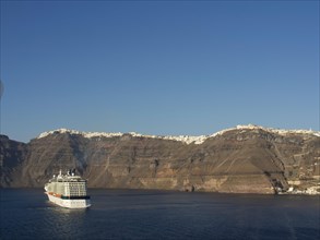 A cruise ship sails near the coast of a village with white buildings, The volcanic island of