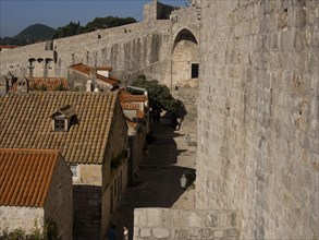 View of a medieval town with old stone buildings and tiled roofs lined by a historic wall, the old
