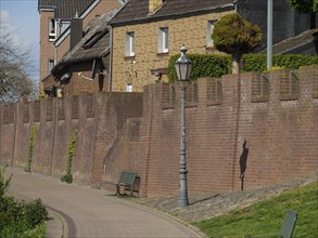 Pavement along a brick wall with houses behind and a street lamp in the foreground, rhine promenade