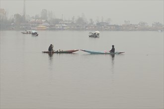 Two people on boats in a foggy lake with distant houses barely visible