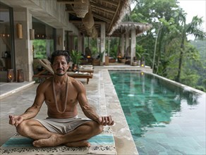 Ein Mann meditiert vor einem Infinity-Pool in einem tropischen Resort, umgeben von ueppiger