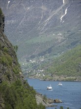 A river flows between mountains, on which several boats sail, spring at a fjord with green trees,