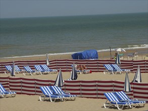 Beach with several blue and white striped sun loungers and parasols, paved with red partitions and