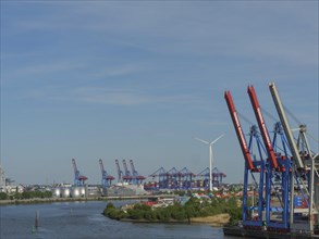 Harbour landscape with cranes, wind turbine and containers, surrounded by water and trees, large