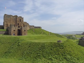 Old castle ruins on a grassy hill under a blue sky on a sunny day, old ruins by the sea in the