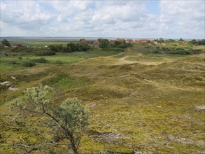 View of a distant village behind hilly, green landscape and meadows under a cloudy sky, Baltrum