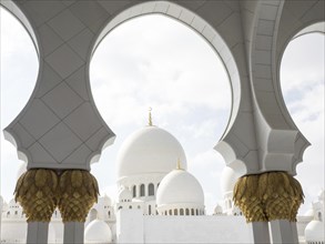 White and gold mosque with magnificent arches and domes, under a cloudy sky, radiates spiritual