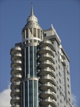 Single modern high-rise building with striking architecture and balconies against a blue sky,
