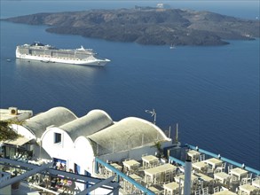View of a white cruise ship in the blue sea near an island with white architecture in Santorini,
