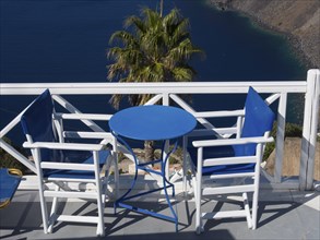 Two white chairs and blue table on a balcony with sea view and palm tree in the background, The