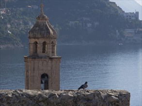 A bell tower with a dove in the foreground, the sea and mountains in the background, a peaceful