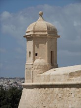 Historic sandstone tower rises against the blue sky in front of a town, Valetta, Malta, Europe