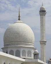A white mosque with a prominent dome and minaret set against a partly cloudy sky