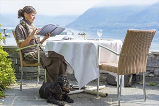 Elegant Woman with Her Dog in an Outdoor Restaurant with Mountain View and Lake Maggiore and