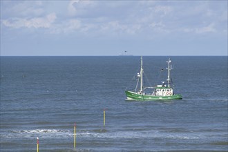 A green ship moves on the calm sea, accompanied by a clear blue sky with clouds, Spiekeroog,