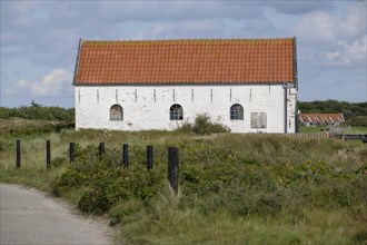 White church with red tiled roof in a wide meadow landscape under a slightly cloudy sky,