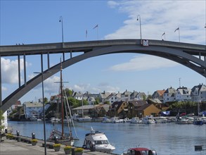 A large bridge over a waterway, including boats and a sailing ship, surrounded by urban houses and