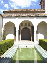 An inner courtyard with archways and a water basin that reflects the architecture and the sky,