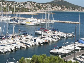 Marina full of boats with a long pier surrounded by green countryside and coastal development under