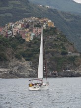 A sailing boat on the sea, against the backdrop of a mountain village with colourful buildings and