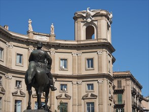 Close-up of an equestrian statue in front of a historic building with sculptures under a clear blue