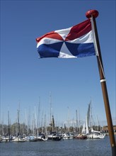 Harbour with many sailing boats and a red-white-blue flag in the foreground under a clear sky,
