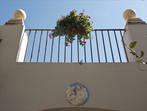 Small balcony with flowers in the courtyard, decorated with a religious image against a blue sky,