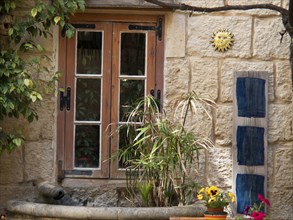 A sunny stone wall spans a window, surrounded by plants and decorations, the town of mdina on the