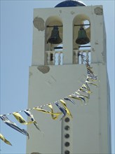 A white bell tower with hanging flags under a blue sky, The volcanic island of Santorini with blue