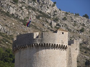Round fortress tower with a flag on a rocky hill under a blue sky, the old town of Dubrovnik with