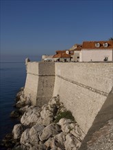 Historic fortress wall on a rocky coastline with houses overlooking the calm blue sea, the old town