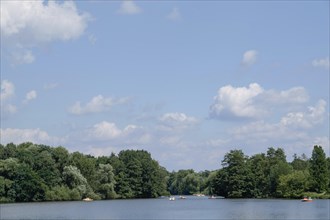 A lake with small boats, surrounded by trees and a slightly cloudy sky, small lake with trees and