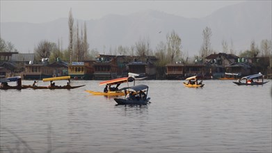 Several boats on a lake surrounded by traditional houses and trees under a misty sky