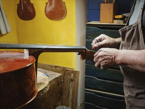 Craftsman stringing a musical instrument, possibly a violin, in a traditional workshop