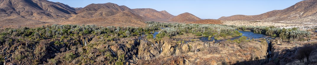 Panorama, Kunene River with green vegetation in dry red mountain landscape, waterfall and African