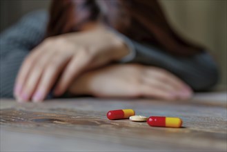 Medicinal drugs on a table with a drugged or passed out woman in the background. Concept for drug