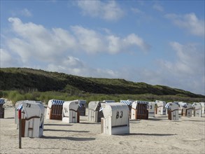 Row of beach chairs in the sand with a cloudy sky above, Spiekeroog, Germany, Europe