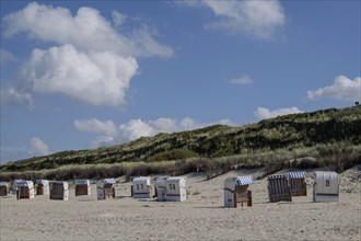 Row of beach chairs on a sandy beach in front of dunes under a blue sky with clouds, Spiekeroog,
