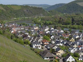 A picturesque village showing many houses, a river and surrounding hills in a green landscape,