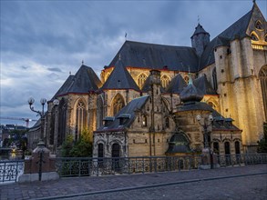 A gothic church at night with lighting, surrounded by old buildings and cobbled streets, historic